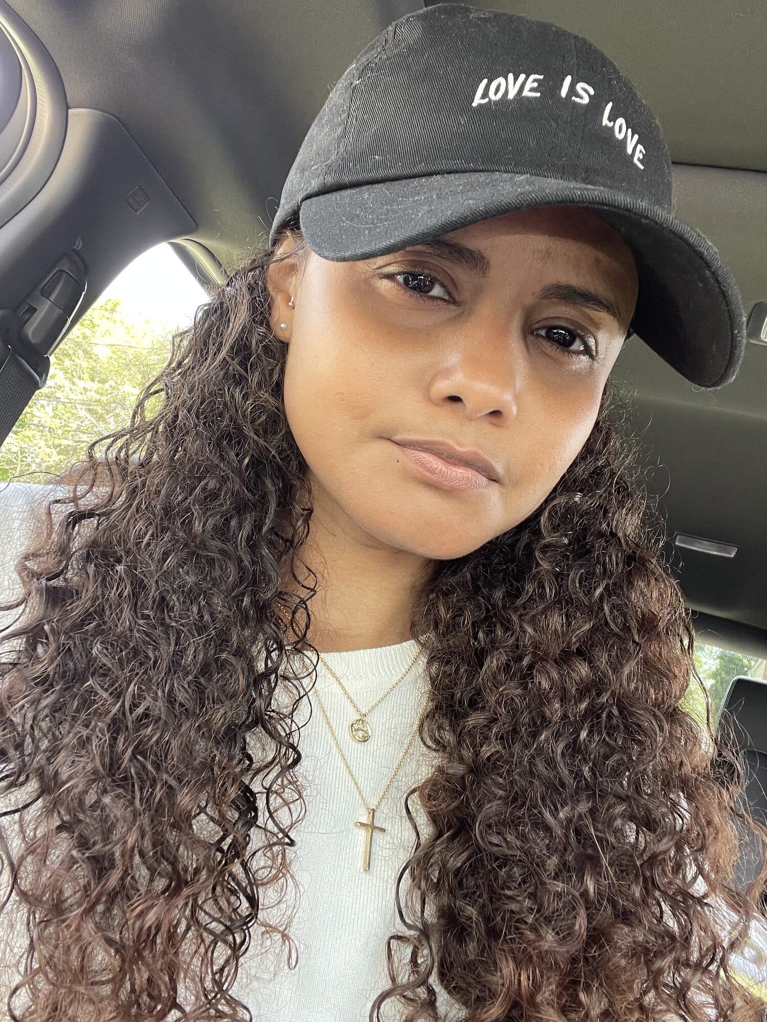 Amorette wearing a Love Is Love cap and a gold cross necklace